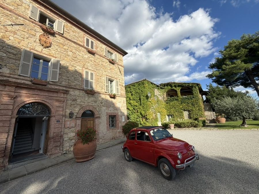 A little red Fiat parked outside a stone farmhouse in Tuscany